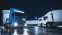 Blue Semi-Truck with Cargo Trailer Drives Off From Overnight Parking Space where Other Trucks are Standing. Long Haul Truck Leaves Parking Lot, Transporting Cargo / Goods Across Continent. Rainy Night